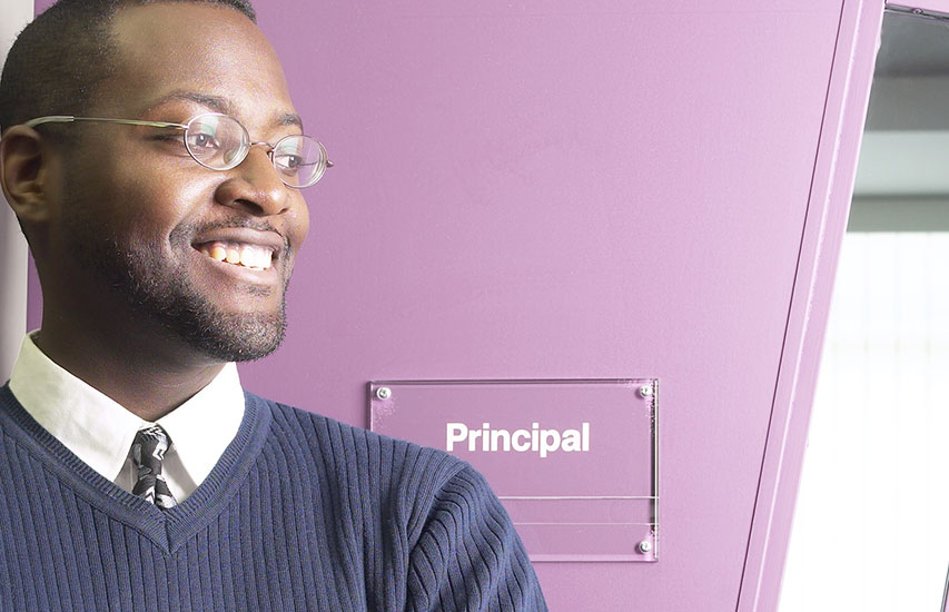 The Curry College Principal and Supervisor Licensure Program (PSL) is represented by a principal in front of his school's office