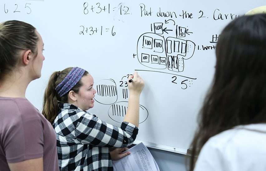 Students at the whiteboard pursuing a Mathematics Education degree from Curry College