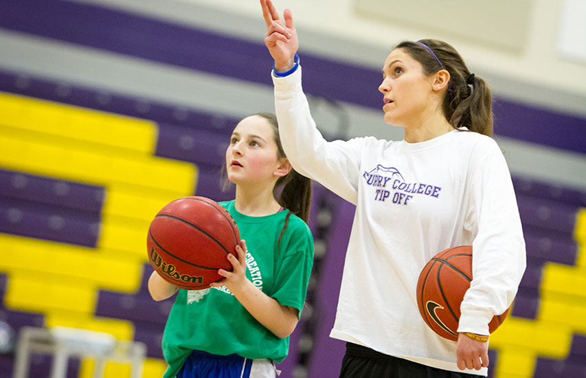 A Curry College student mentors a young athlete on the basketball court representing the Sports/Youth Recreation and Programming minor and concentration
