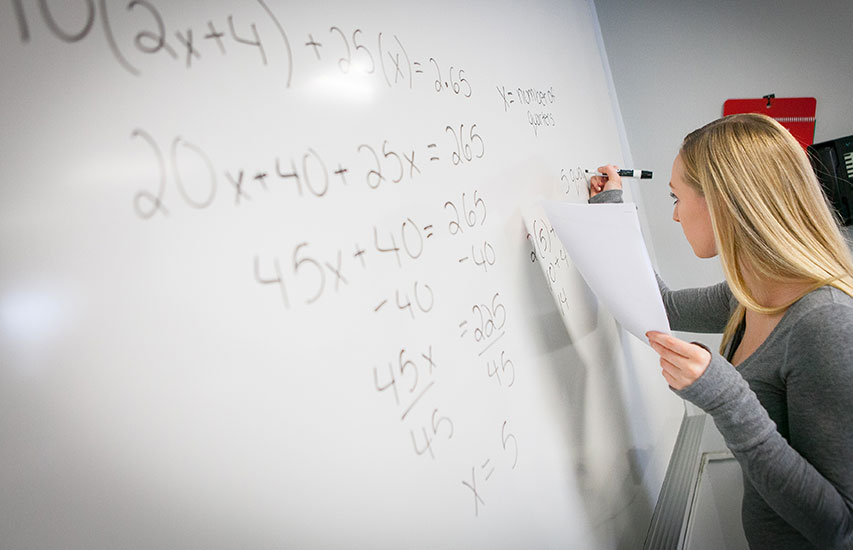 Student works out an equation at the whiteboard while pursuing a Mathematics minor at Curry College