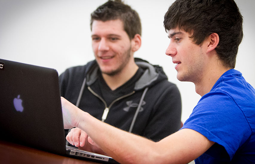 Students collaborate on a laptop while pursuing an Applied Computing minor at Curry College