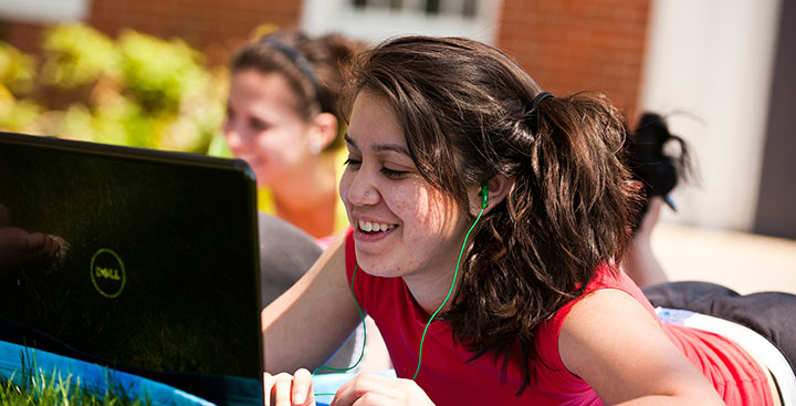 A Curry College student on her laptop laying in the Academic Quad