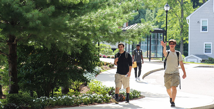 Curry College student smiles and waves as he walks to class with a friend